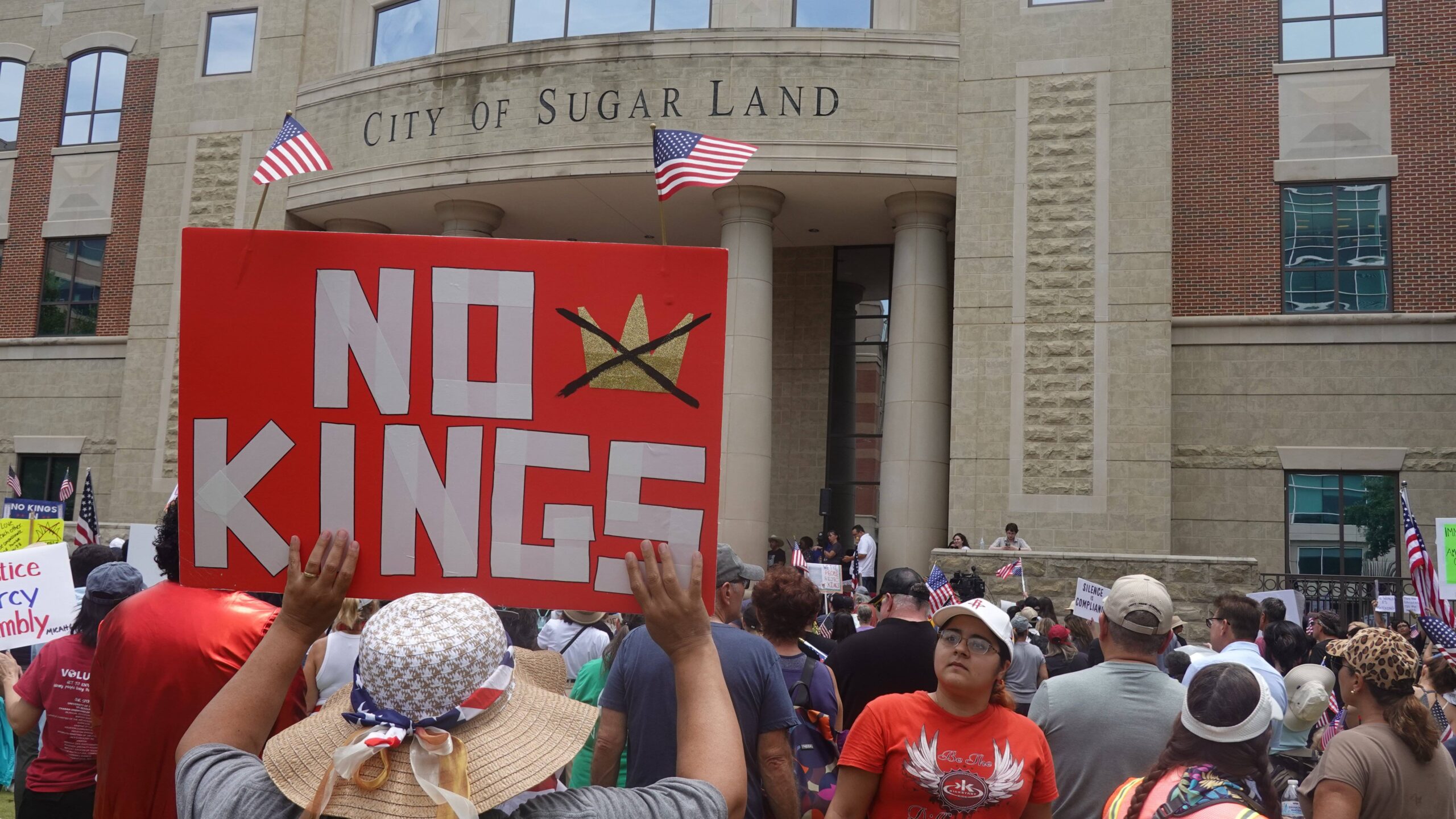 Devant l'hôtel de ville de Sugar Land, au Texas, la couronne barrée s'affiche entre deux drapeaux américains : dans cet État remporté deux fois par Trump, la contestation emprunte les emblèmes patriotiques. Photo : Xu Jianmei / Xinhua