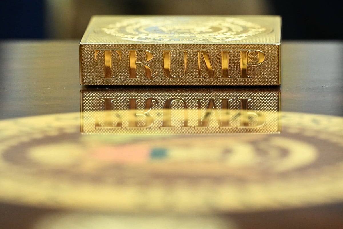 A gilded coaster engraved with the presidential seal and the name “TRUMP,” laid on a table in the Oval Office, reflecting in the varnished surface. White House photo