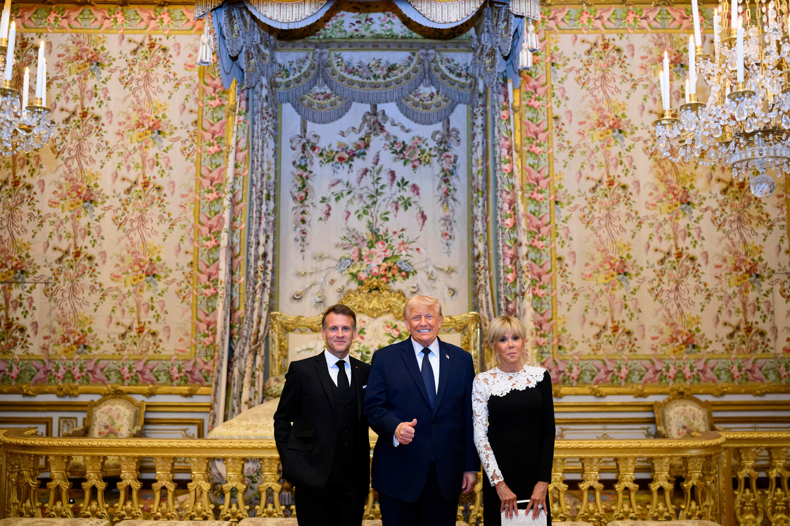 The raised thumb in the Queen’s Chamber, before Marie-Antoinette’s canopied bed, the Las Vegas gesture meeting the Old Regime’s décor.