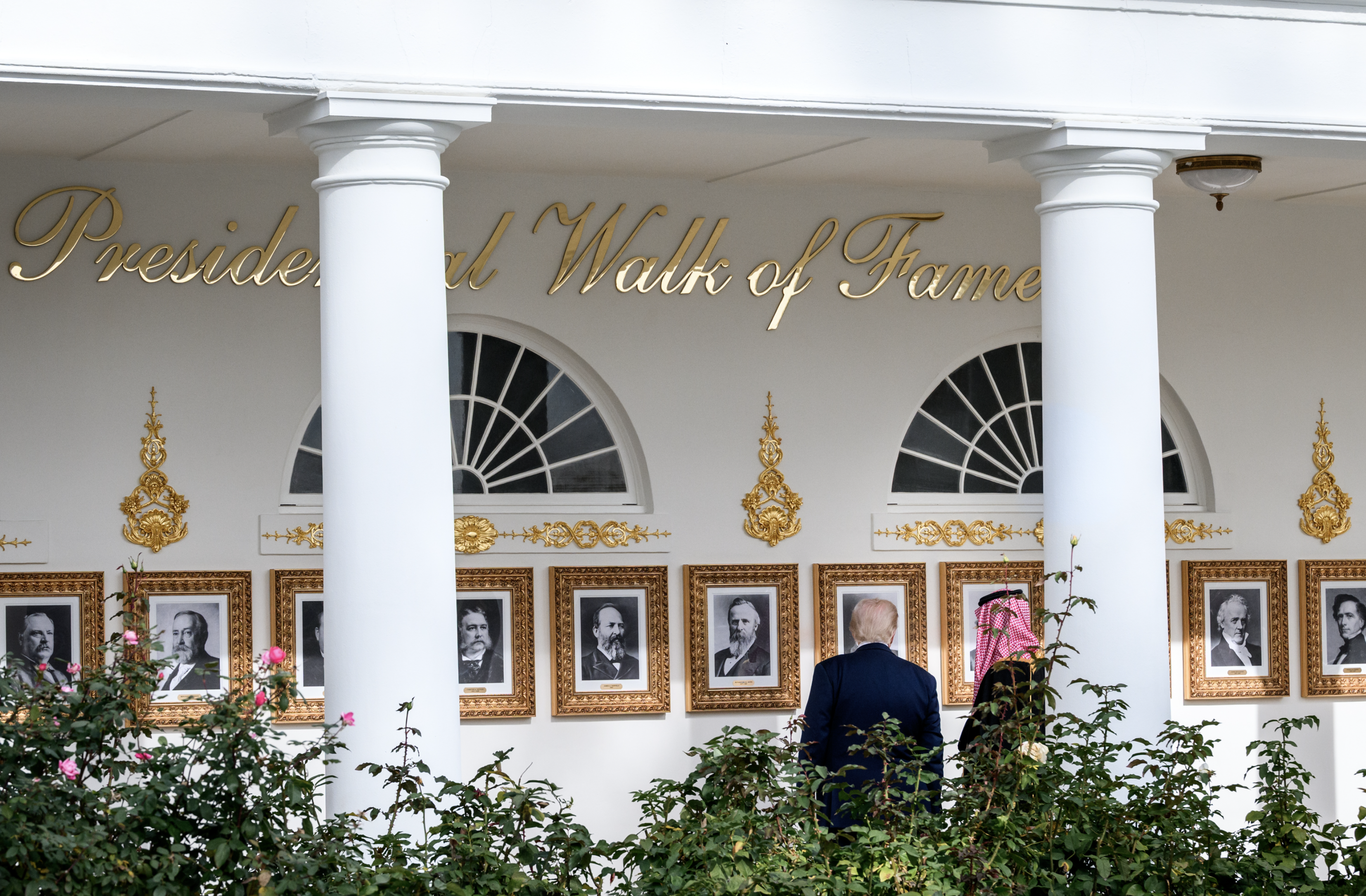Donald Trump and his guest stroll along the Rose Garden colonnade, redesigned into a 'Presidential Walk of Fame': portraits of presidents in gilded frames under a cursive gold-letter sign. White House official photo