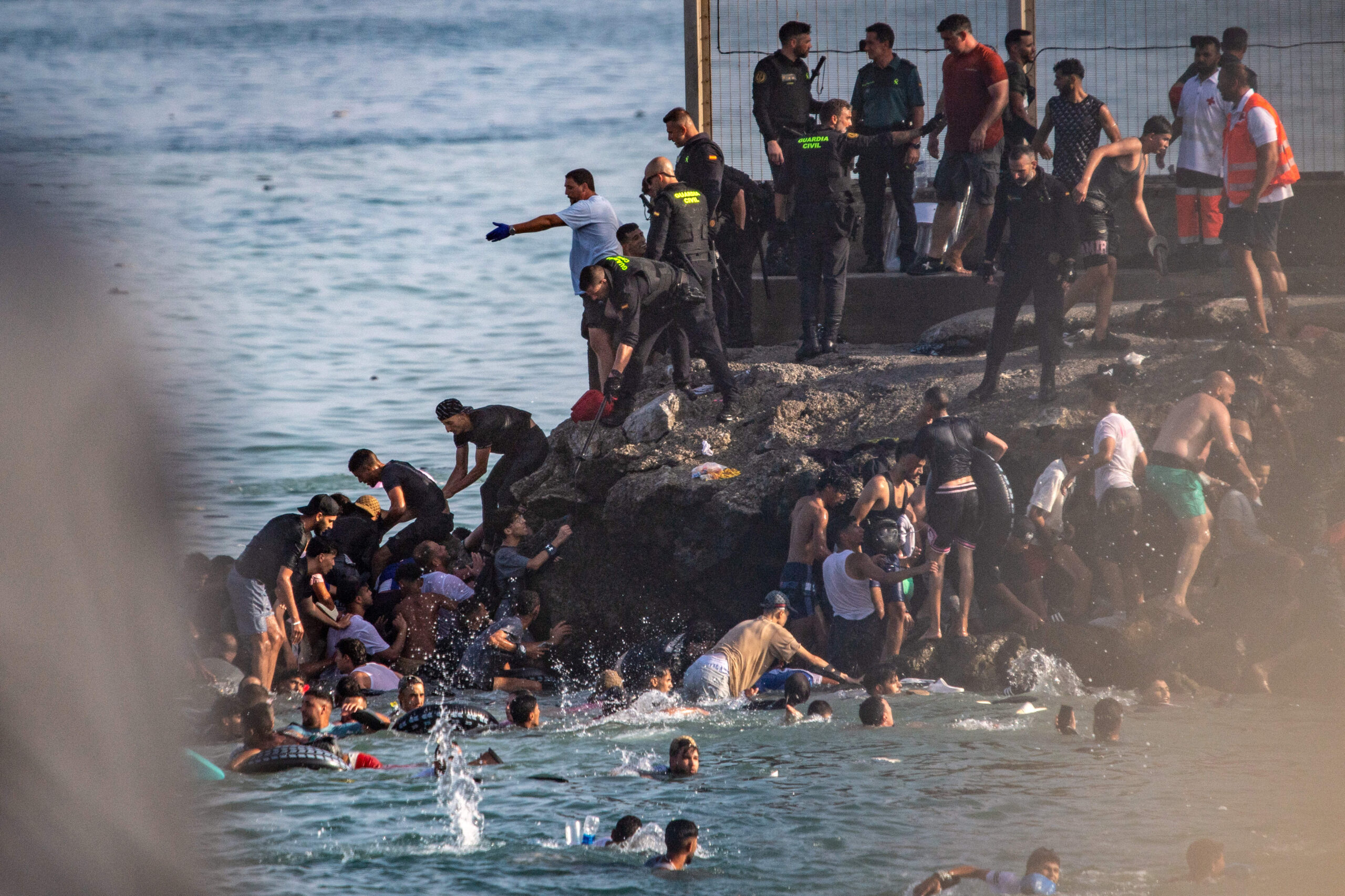 Sur les rochers de la jetée, la frontière devient sauvetage : la Guardia Civil et la Croix-Rouge aident à sortir de l'eau les migrants après la traversée. © AP Photo/Antonio Sempere/SIPA