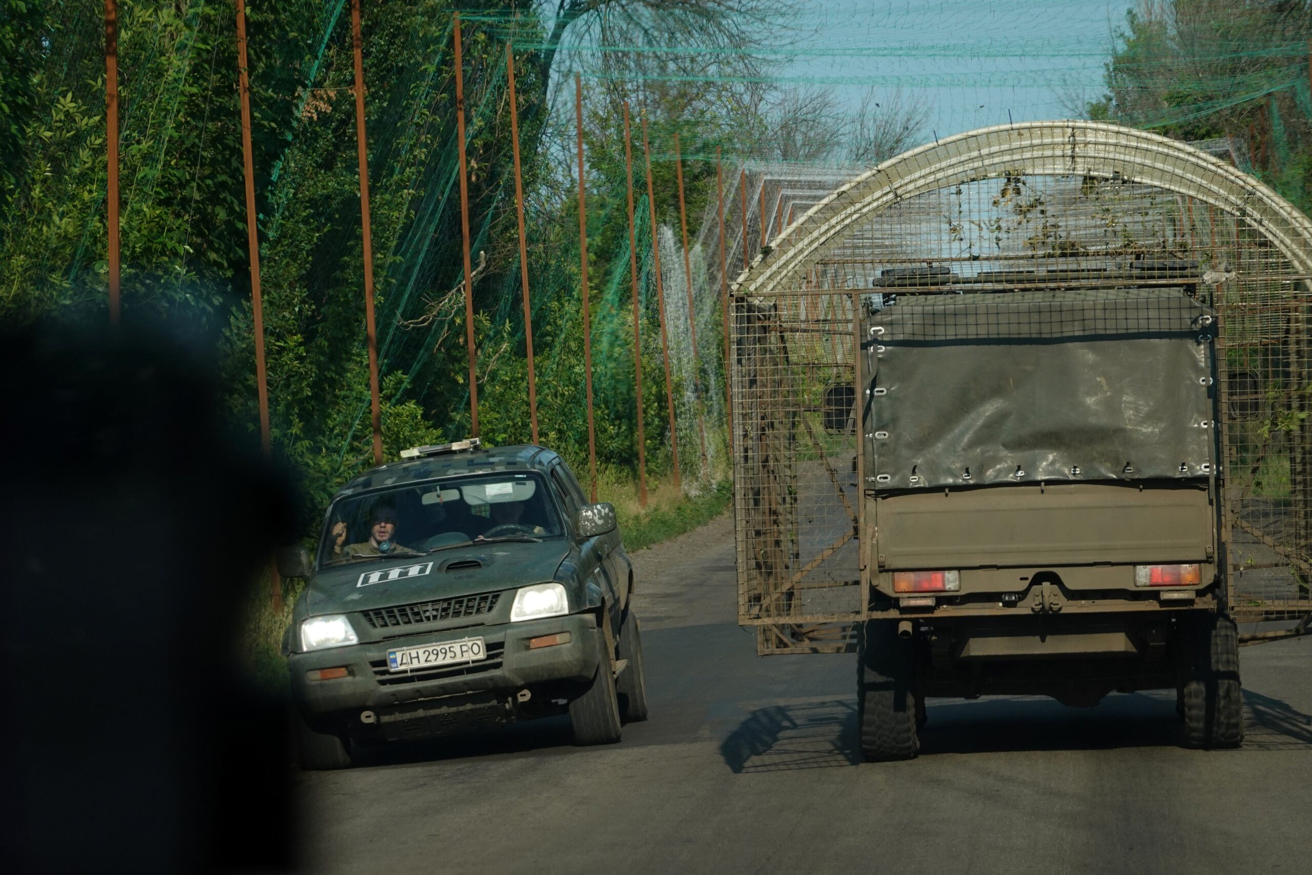 Deux véhicules militaires, dont un camion équipé d'une cage anti-drone, se croise sous la canopée d'un filet anti-drone non loin de Kramatorsk, le 7 juillet 2026.
