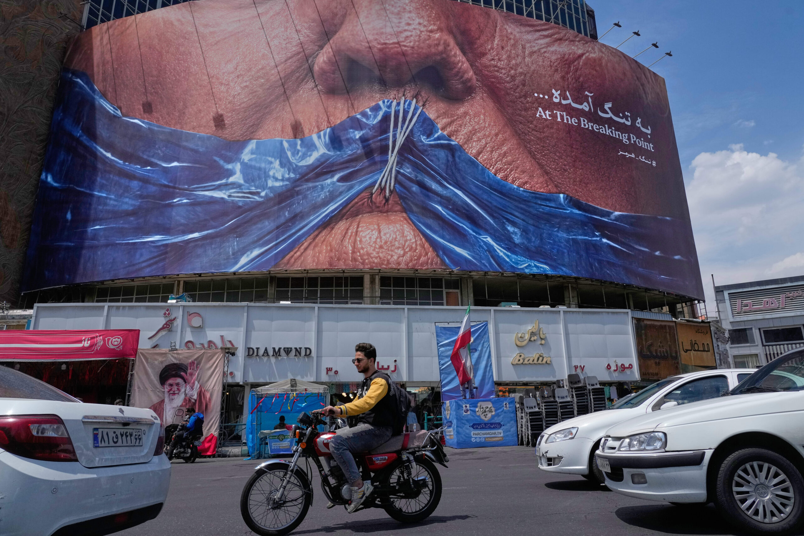 Donald Trump is represented gagged with a gag shaped like the Strait of Hormuz, on a placard in downtown Tehran, May 2, 2026.