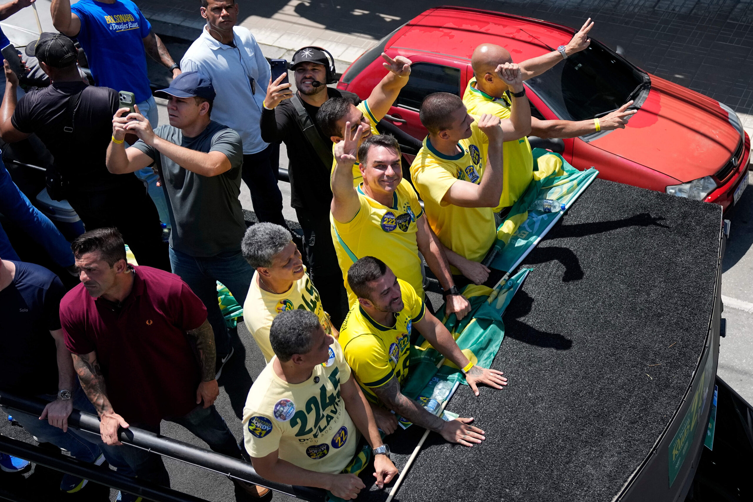 Le bras tendu, Flávio Bolsonaro fait un signe de la main en forme de « V » pour signifier « Victoire ».